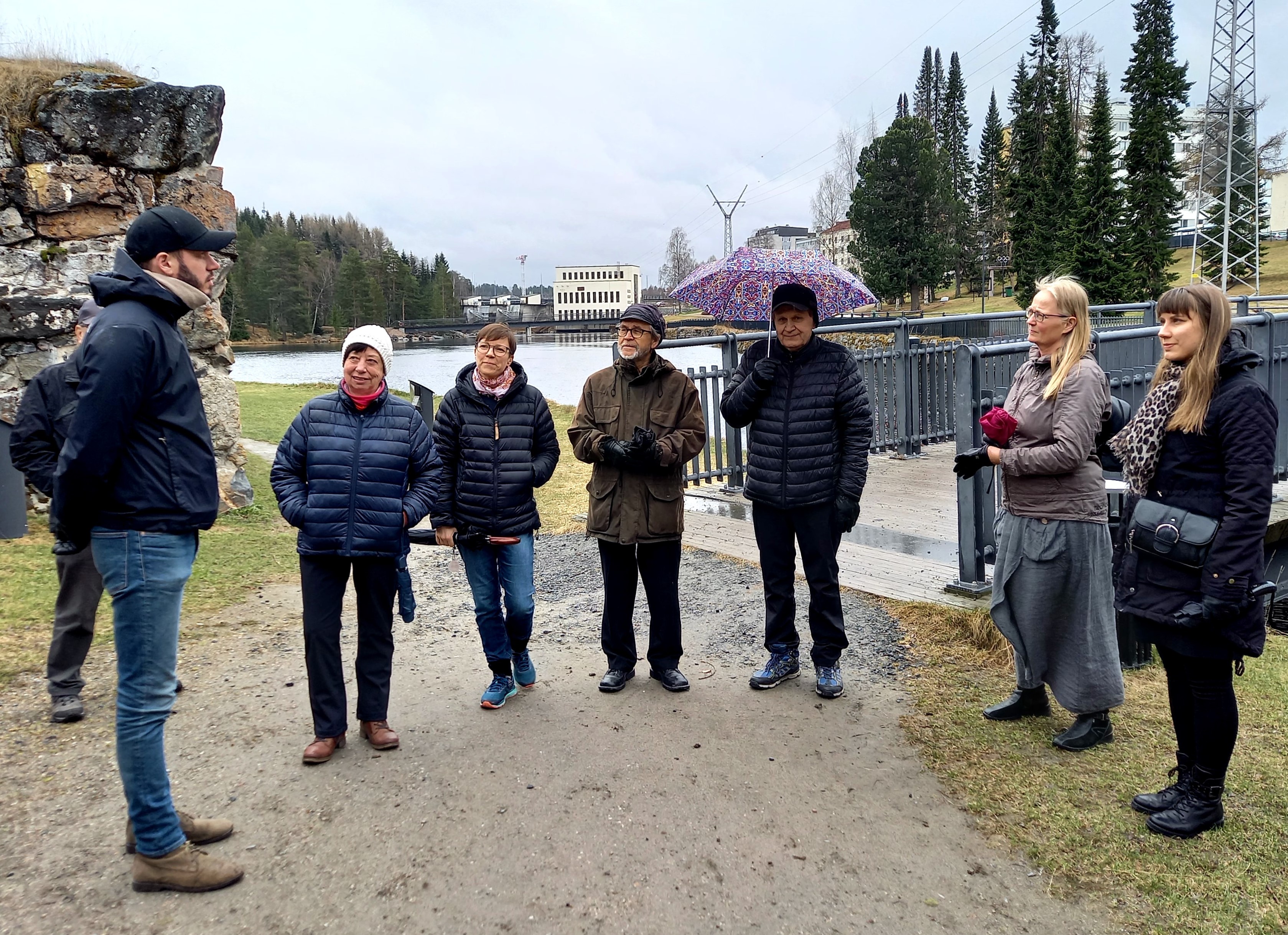 ihmisiä seisomassa joen rannalla takana voimalaitos