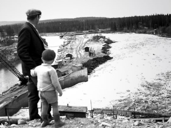 Mies ja poika katsovat alhaalla olevaa voimalaitostyömaata ja jokea