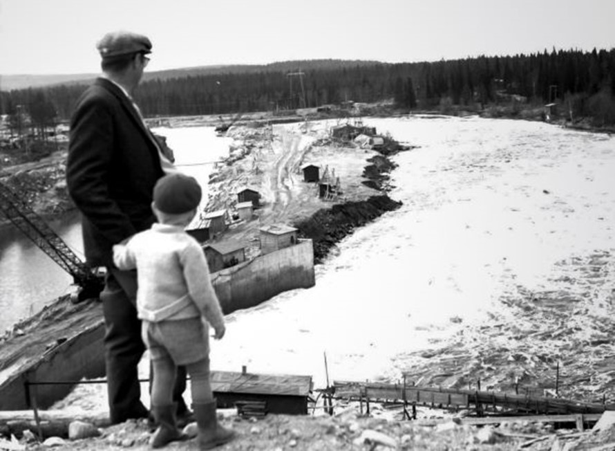Mies ja poika katsovat alhaalla olevaa voimalaitostyömaata ja jokea